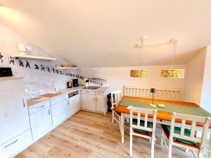 Moderne Küche mit Tisch und Stühlen in einem Raum In einem Raum steht eine Küche mit einem Esstisch und Stühlen. Die Wand zeigt Figuren und es gibt Küchenutensilien.