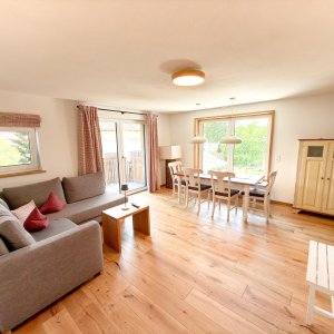 Wohnzimmer mit Esstisch und Terrasse Ein Raum mit einem Sofa und einem Esstisch. Fenster geben Licht und Zugang zur Terrasse. Möbel aus Holz sind sichtbar.