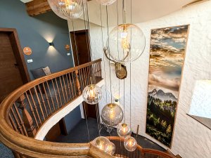 Treppenhaus mit modernen Lampen und Holzgeländer Das Treppenhaus zeigt eine Holztreppe mit einer Vielzahl von lampen und einem großen Bild an der Wand.