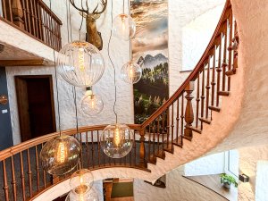 Treppenhaus mit großen Lampen und einem Geweih Das Treppenhaus zeigt eine Holztreppe und runde Lampen. An der Wand hängt ein Geweih. Fenster lassen Licht herein.
