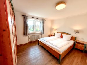 Schlafzimmer in einer Wohnung mit zwei Betten Das Schlafzimmer zeigt zwei Betten, einen Schrank und einen Fensterblick. Es ist tagsüber und hat Holzfußboden.