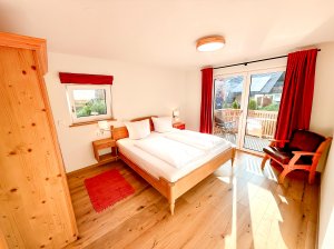 Helles Zimmer mit Blick auf den Balkon In einem ruhigen Raum gibt es ein Bett, einen Sessel und Fenster. Der Balkon führt nach draußen.