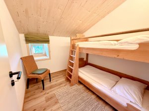 Schlafzimmer mit Etagenbett und einem Stuhl In einem Zimmer sind ein Etagenbett und ein Stuhl zu sehen. Licht kommt durch das Fenster. Der Boden ist aus Holz.