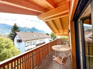Balkon mit Blick auf die Berge in der Stadt Ein Balkon zeigt einen Blick auf Berge und Häuser während des Tages. Die Sonne scheint und der Himmel ist blau.