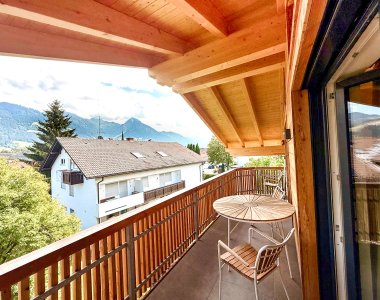 Ein Balkon zeigt einen Blick auf Berge und Häuser während des Tages. Die Sonne scheint und der Himmel ist blau.
