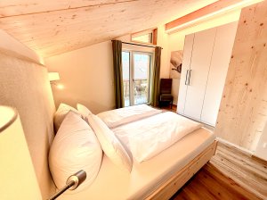 Das Zimmer hat ein Bett und einen Balkon In einem Zimmer mit einem Bett und einem Balkon steht eine Lampe. Die Wände sind hell und es gibt Holzfußboden.