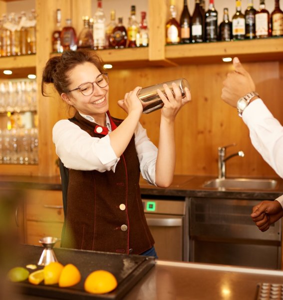 Eine Mitarbeiterin bekommt von einem anderen Mitarbeiter im Hotel Oberstdorf gezeigt, wie Cocktails gemixt werden
