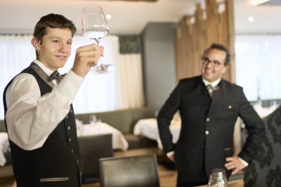 Ein Azubi der Allgäu AzubiTopHotels prüft die Sauberkeit von Gläsern während sein Ausbilder daneben steht