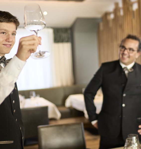 Ein Azubi der Allgäu AzubiTopHotels prüft die Sauberkeit von Gläsern während sein Ausbilder daneben steht