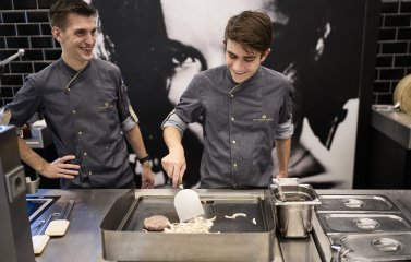 Ein Koch und sein Koch-Azubi braten gemeinsam einen Burger