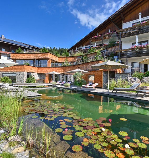 Blick auf den Naturbadeteich und die Außenansicht im Sommer im Biohotel Eggensberger in Füssen, Hopfen am See.