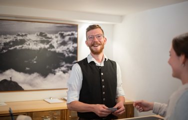 Ein Azubi arbeitet an der Rezeption und lacht in die Kamera