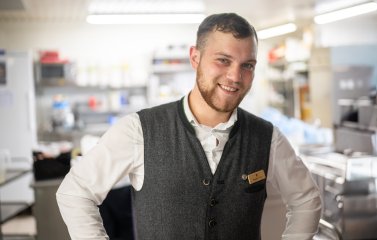 Ein Azubi vom Service holt etwas aus der Küche und lacht in die Kamera
