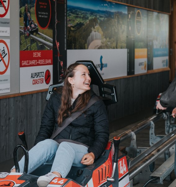 Eine Mitarbeiterin vom PANORAMA Allgäu-Spa-Resort in Rückholz hockt während des Mitarbeiterausfluges in einem Alpspitz Coaster