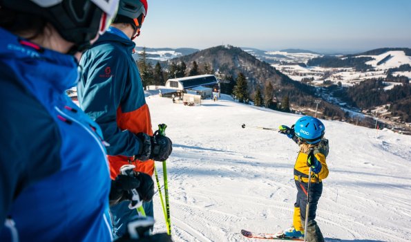 Eine Familie genießt das Skifahren auf einem schönen Hang. Ein Kind zeigt auf einen Schneeball im Winterwunderland.