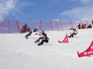 Sportler fahren in einem Schnee-Snowboardrennen den Hang hinunter. Die Veranstaltung findet an einem sonnigen Tag statt.