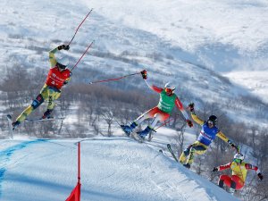 Vier Skifahrer nehmen am Wettbewerb teil und springen über eine Sprungschanze in verschneiten Bergen an einem sonnigen Tag.