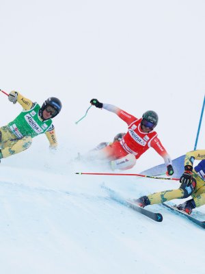 Drei Skifahrer rasen bei einem Wettkampf in den Alpen auf einer verschneiten Piste.