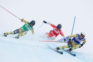 Drei Skifahrer rasen bei einem Wettkampf in den Alpen auf einer verschneiten Piste.