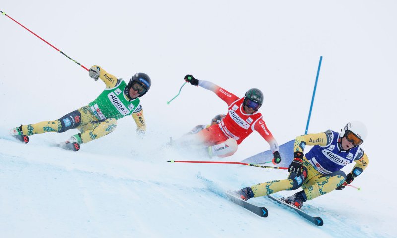Drei Skifahrer rasen bei einem Wettkampf in den Alpen auf einer verschneiten Piste.