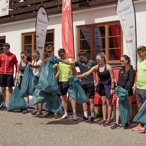 Eine Gruppe von Jugendlichen sammelt Müll in der Natur bei einem Event. Sie tragen alle Müllsäcke und arbeiten zusammen.