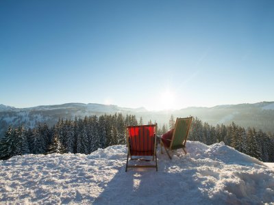 Zwei Liegestühle stehen auf einem verschneiten Hügel und bieten eine herrliche Aussicht auf die Winterlandschaft.