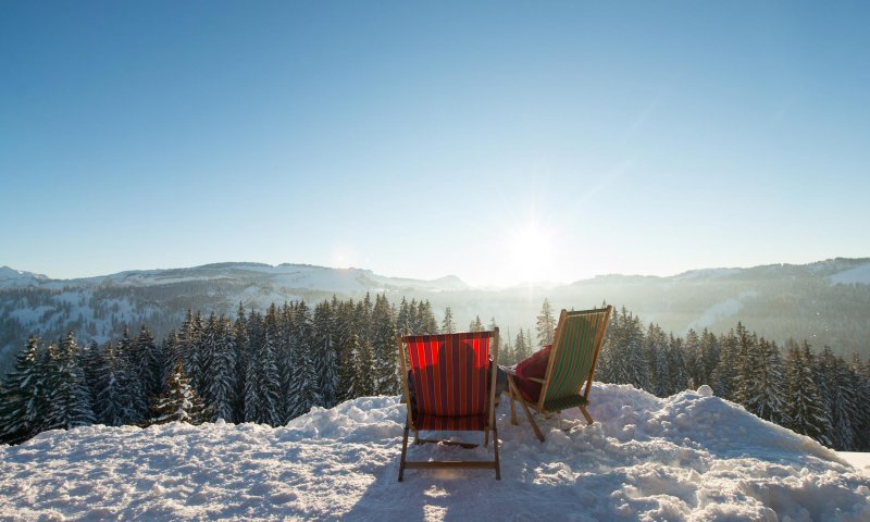 Zwei Liegestühle stehen auf einem verschneiten Hügel und bieten eine herrliche Aussicht auf die Winterlandschaft.