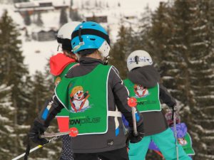 Kinder lernen Skifahren in einer Winterlandschaft. Sie tragen helle Kleidung und Spaß steht im Vordergrund.