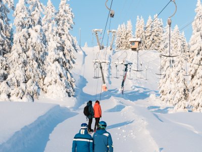 Drei Skifahrer gehen durch den verschneiten Wald zur Seilbahn, um einen aufregenden Skitag zu starten.