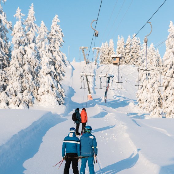 Drei Skifahrer gehen durch den verschneiten Wald zur Seilbahn, um einen aufregenden Skitag zu starten.