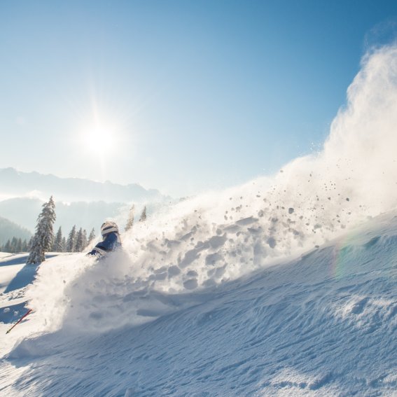 Ein Skifahrer fährt in den Bergen durch den frischen Schnee bei Sonnenschein und klarem Himmel.