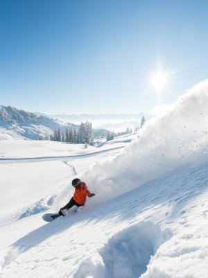 Ein Snowboarder genießt den perfekten Tag im Schnee unter klarem, blauem Himmel und strahlender Sonne.