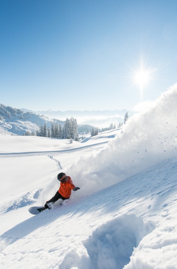 Ein Snowboarder genießt den perfekten Tag im Schnee unter klarem, blauem Himmel und strahlender Sonne.