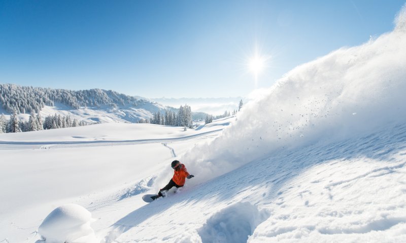 Ein Snowboarder genießt den perfekten Tag im Schnee unter klarem, blauem Himmel und strahlender Sonne.