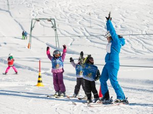 Group von Kindern übt Skifahren mit einem Lehrer auf einem sonnigen Hang in den Alpen. Spaß und Freude am Wintersport sind spürbar.