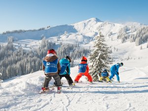 Eine Gruppe von Kindern lernt Skifahren in den verschneiten Bergen an einem sonnigen Wintertag.
