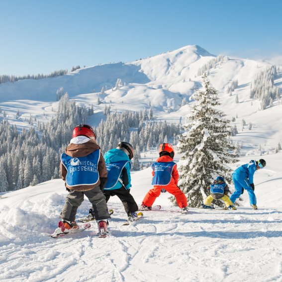 Skifahren mit Kindern in verschneiter Landschaft Eine Gruppe von Kindern lernt Skifahren in den verschneiten Bergen an einem sonnigen Wintertag.