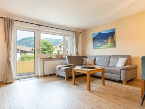 In einem modernen Wohnzimmer steht eine graue Couch, während Sonnenstrahlen durch die Fenster scheinen.