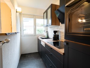 Eine helle, moderne Küche mit schwarzen Schränken und Holzdetails, ausgestattet mit Geräten und Blick nach draußen.