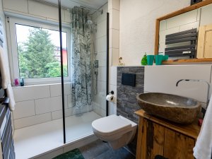 Ein helles Badezimmer mit moderner Glasdusche und eleganten Holzdetails sorgt für eine angenehme Atmosphäre bei der Körperpflege.