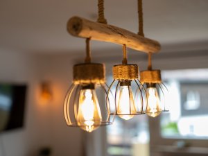 Eine Hängeleuchte mit drei Glühbirnen beleuchtet einen stilvollen Wohnraum in sanften Farben und modernem Design.
