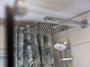 Im Badezimmer sprudelt Wasser aus einem modernen Duschkopf und trifft auf die Fliesen, die geräumig wirken.