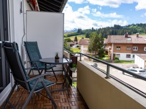 Gemütlicher Balkon mit zwei Stühlen und Tisch, ideal zum Entspannen unter blauem Himmel und grünen Bergen.