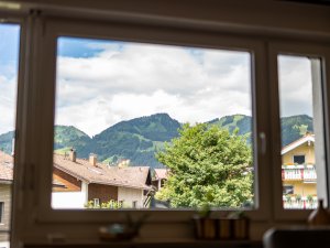 Durch das Fenster ist eine malerische Alpenlandschaft mit Bergen und Bäumen sichtbar. Die Wolken schweben am Himmel.
