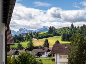 Eine malerische Berglandschaft mit Chalets, Wiesen und majestätischen Gipfeln unter wolkenlosem Himmel in den bayerischen Alpen.