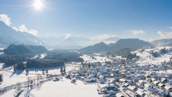 Ein malerisches Tal mit schneebedeckten Dächern und majestätischen Bergen im Hintergrund an einem klaren Wintertag.
