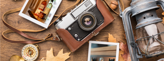 Auf einem Holztisch liegen eine Kamera, Herbstblätter, Eicheln und verschiedene Gegenstände für eine gemütliche Atmosphäre.