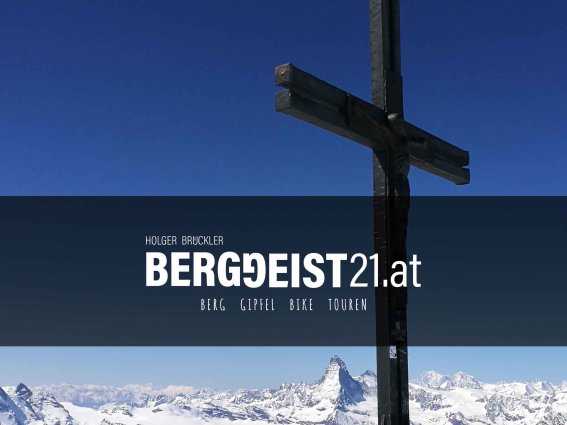 Ein wunderschöner Bergblick mit einem hölzernen Kreuz im Vordergrund unter strahlend blauem Himmel.