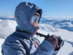 Eine Person mit Kamera steht in der Schneeberglandschaft und fotografiert die beeindruckende Aussicht unter klarem Himmel.