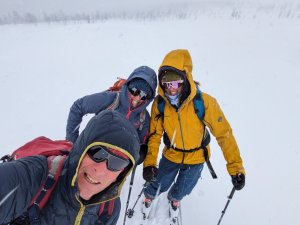 Drei Personen machen eine Schneeschuhwanderung in schneebedeckten Bergen an einem kalten Wintertag.